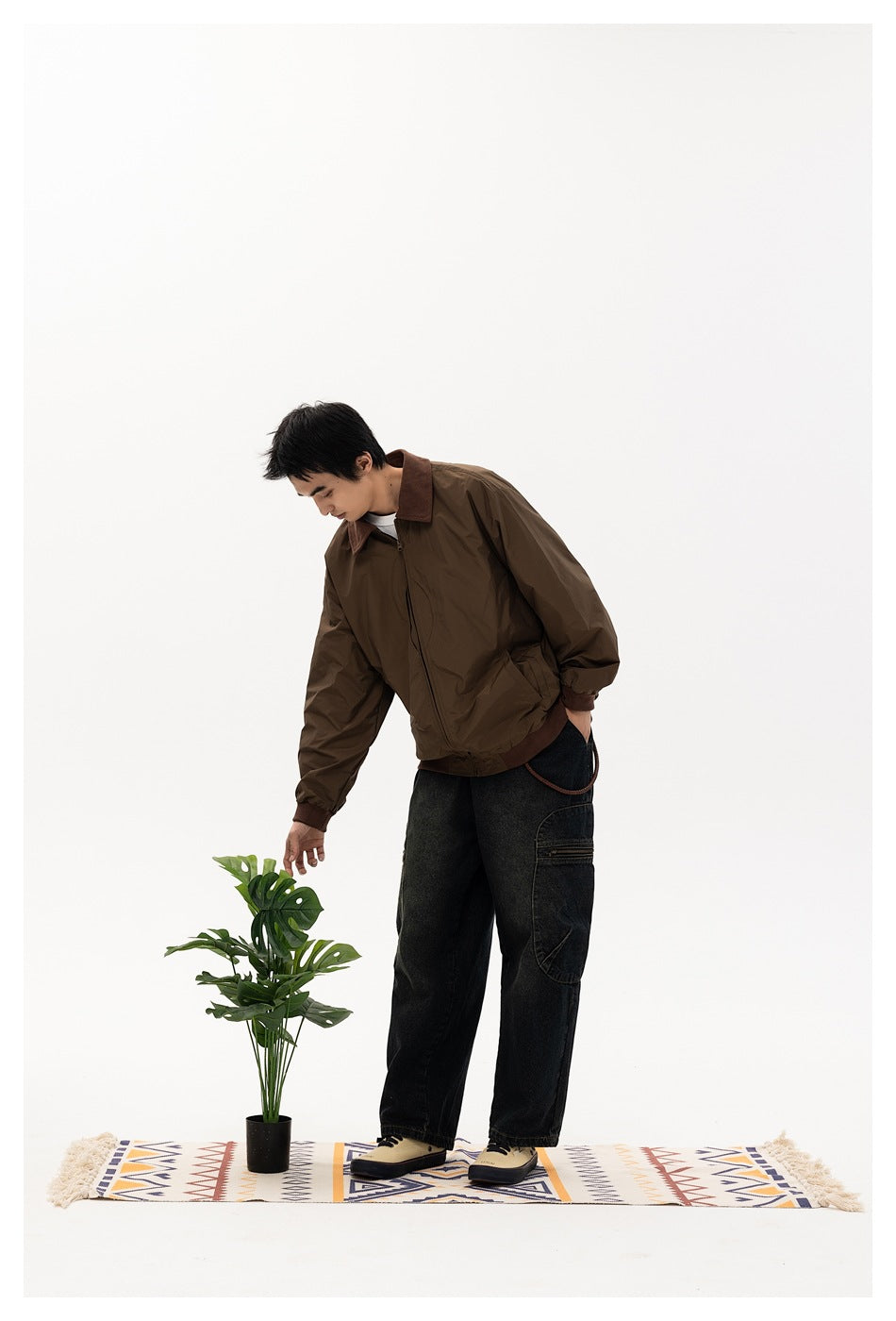 Model bending toward a plant while wearing a dark brown zip-front jacket with a brown collar and cuffs.