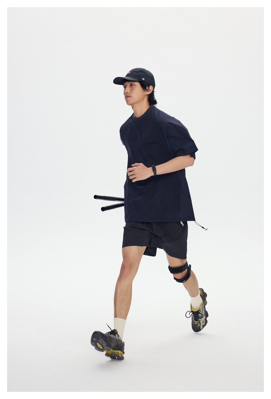 Model wearing a navy short-sleeve shirt and black shorts in a running pose against a white background.