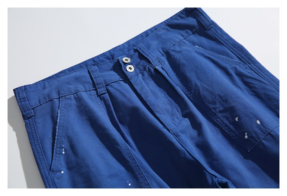 Close-up of royal blue pants showing two-button waistband, belt loops, front pocket and white paint splatters