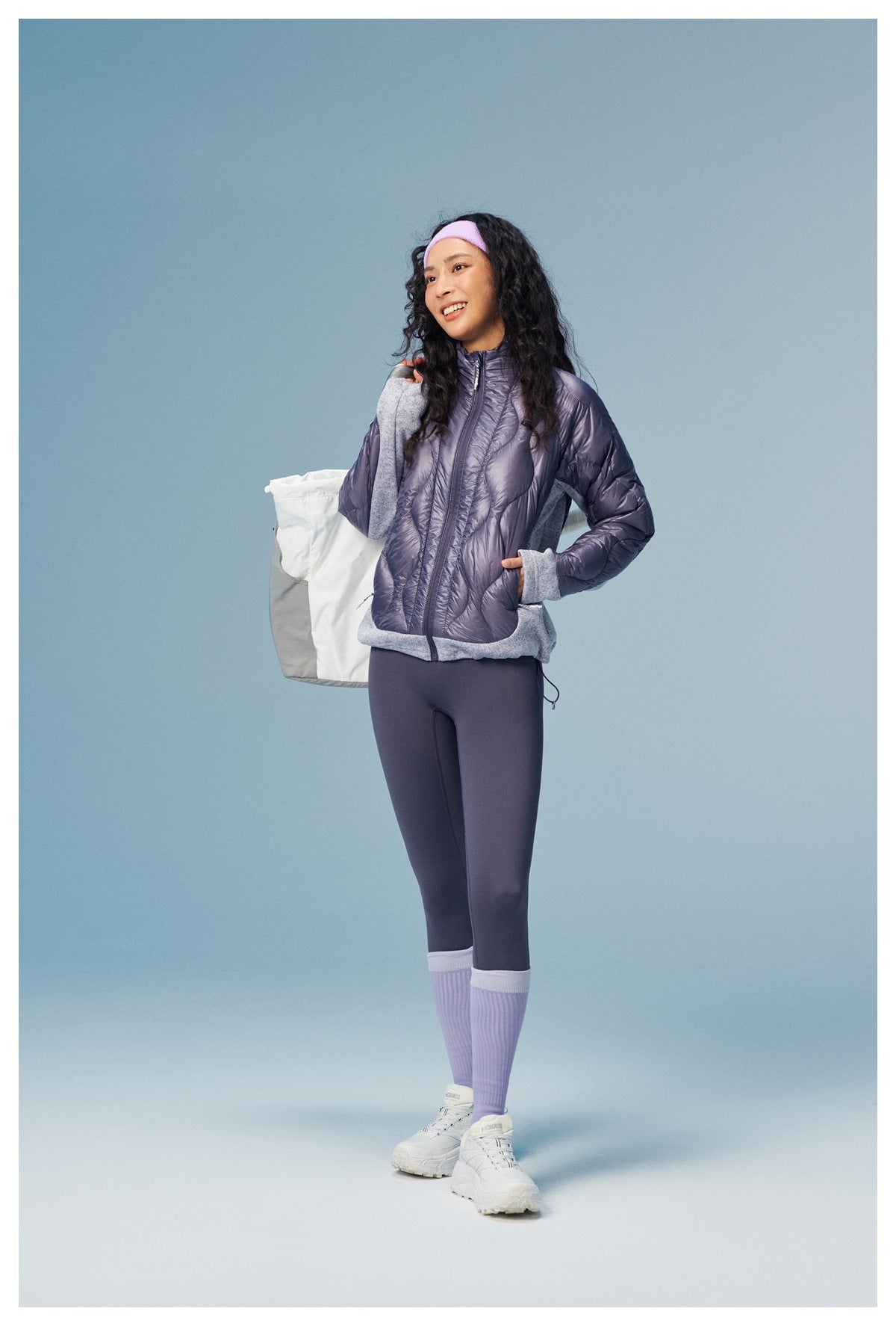 Full-length view of a woman wearing a lavender quilted zip jacket with gray panels and matching leggings.