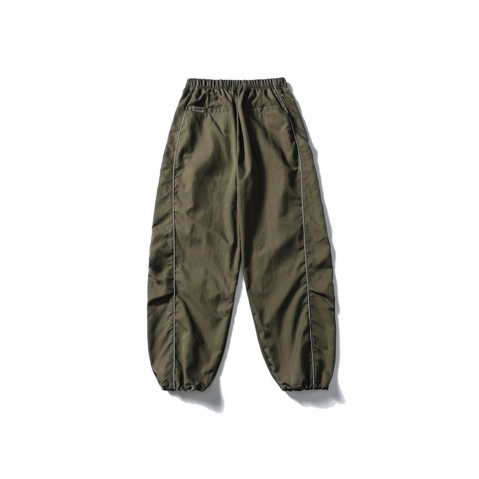 Olive drab relaxed pants shown from the back, with an elastic waist, two pockets, side piping and gathered cuffs.