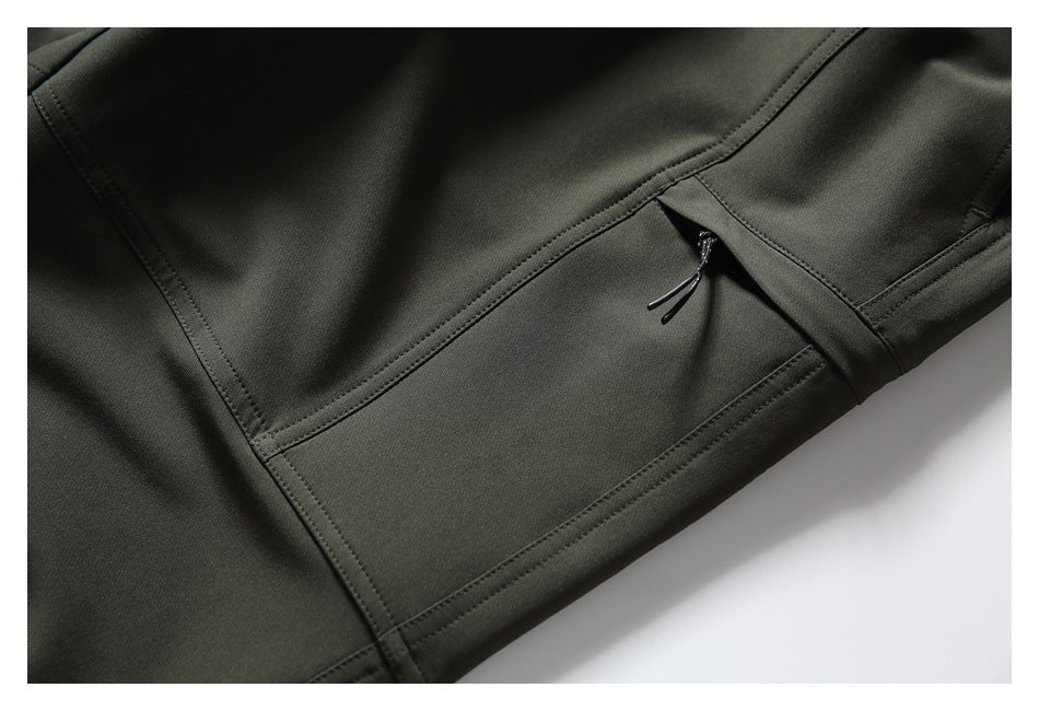 Close-up of a zip pocket with cord pull and stitched paneling on dark olive pants.