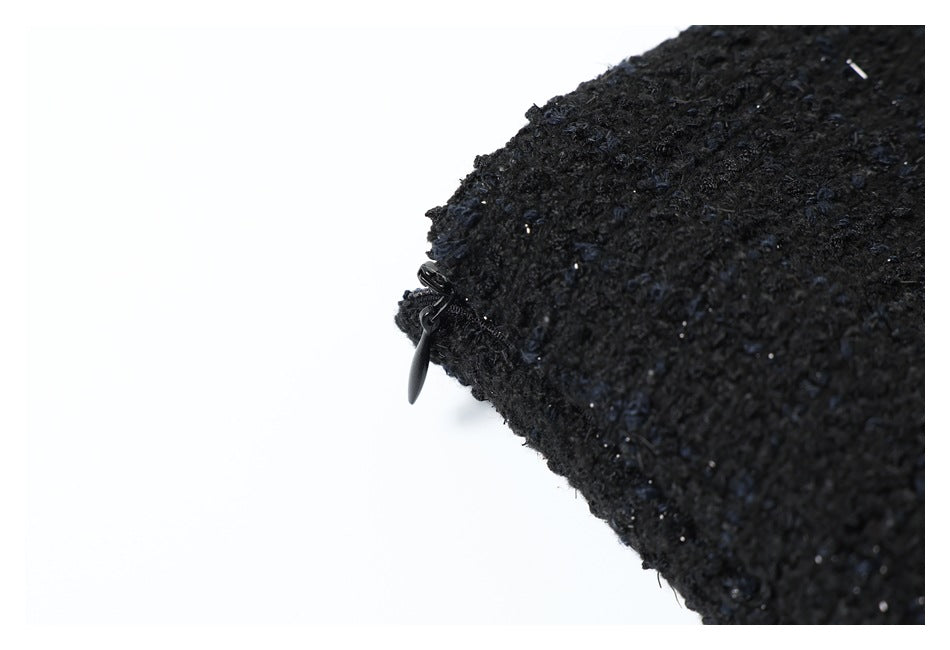 Close-up of a black zipper pull beside the edge of textured black fabric.