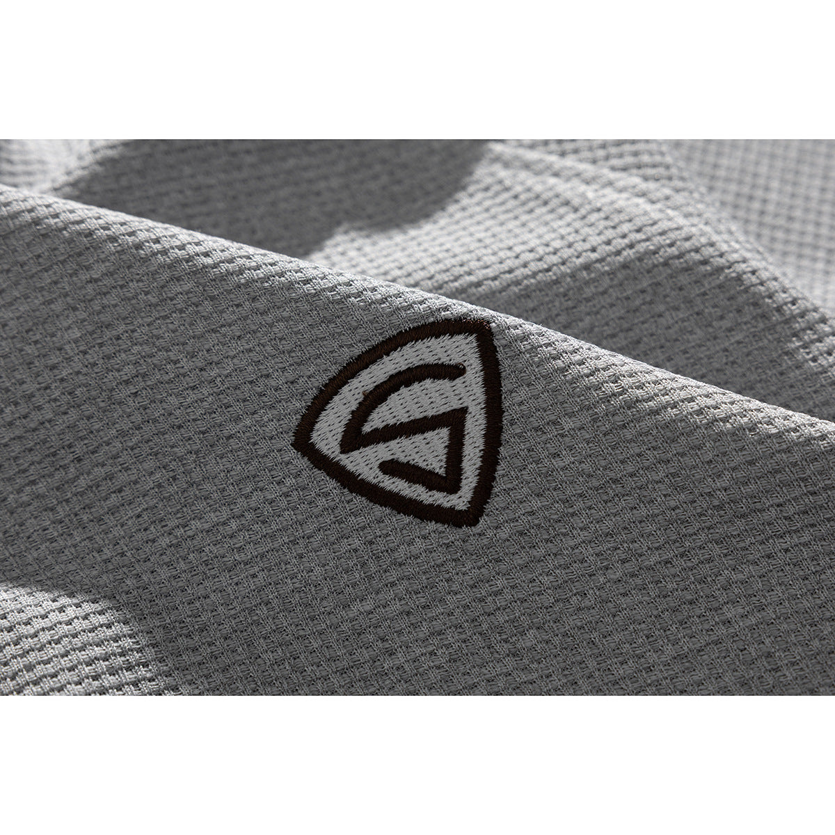 Close-up of a small dark shield-shaped embroidered emblem on light gray textured fabric.