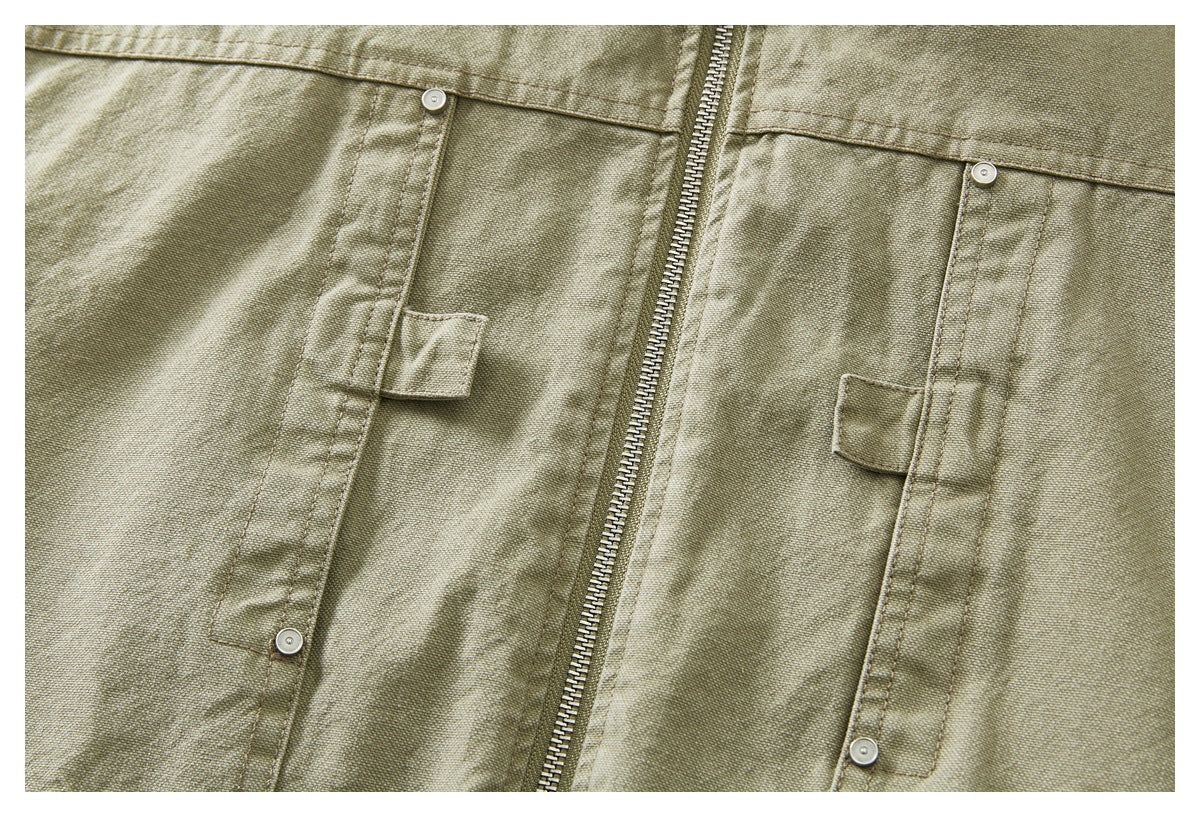 Close-up of an olive khaki jacket front with a metal zipper and snap-button flap pockets.