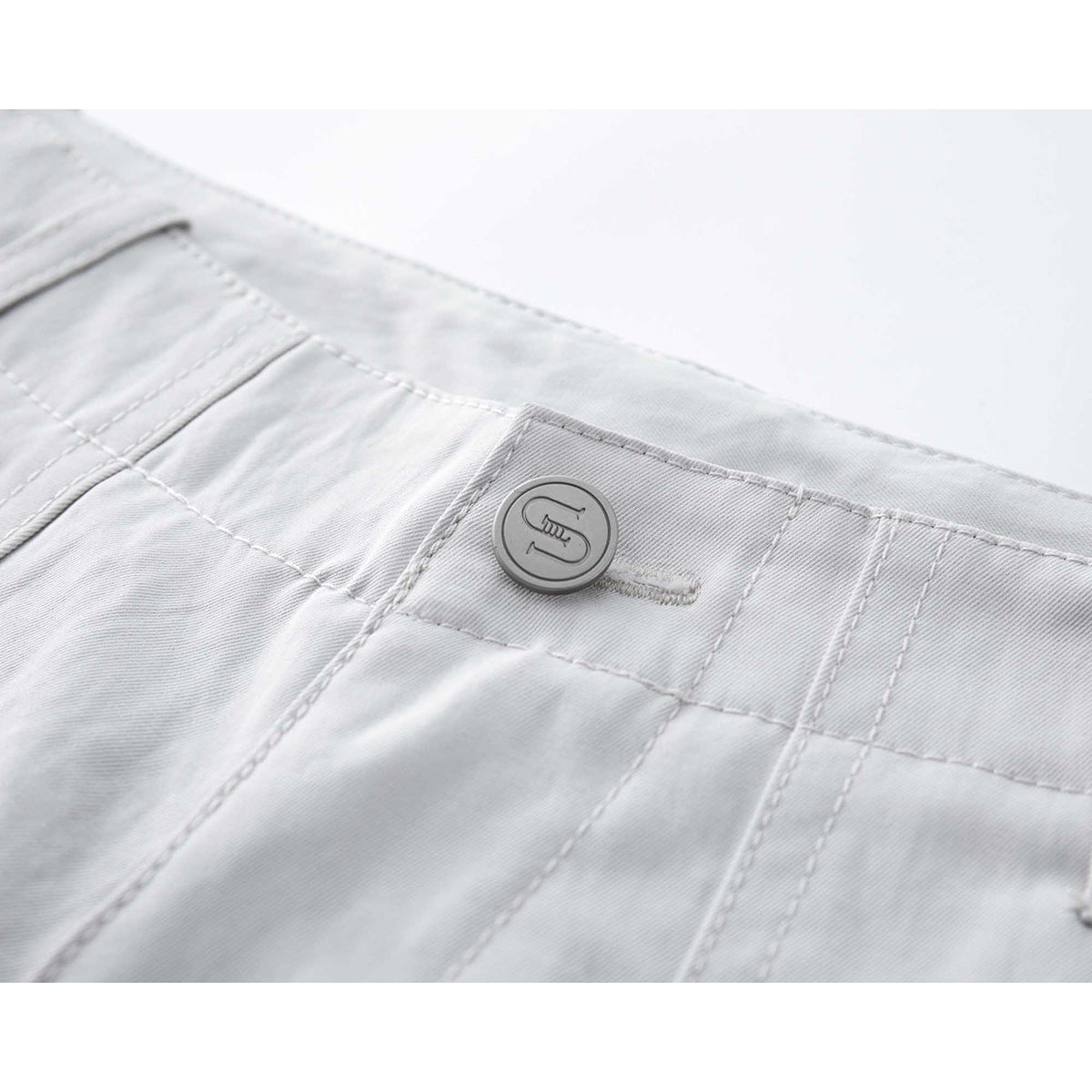 Close-up of white shorts showing the waistband, stitching, and a round engraved button.