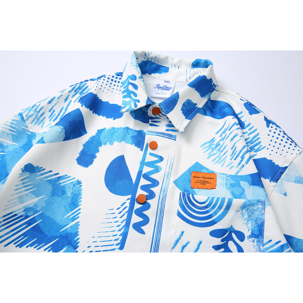 Close-up of a white collared shirt with bold blue abstract prints, orange buttons and a chest pocket.