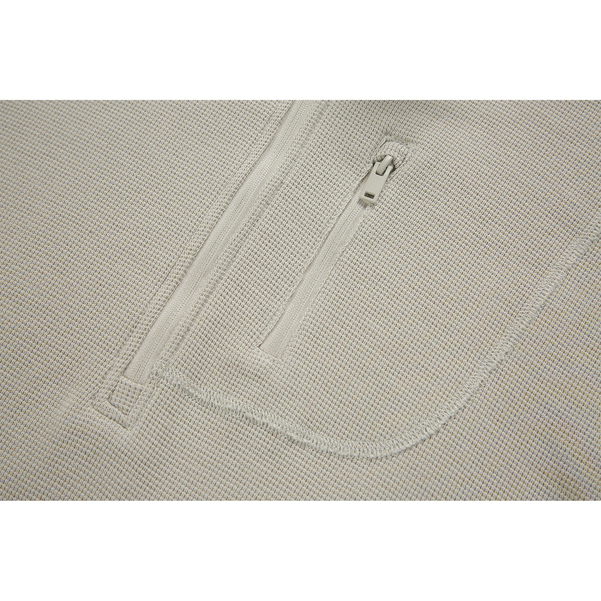Close-up of the light beige pullover's zippered chest pocket and textured fabric.