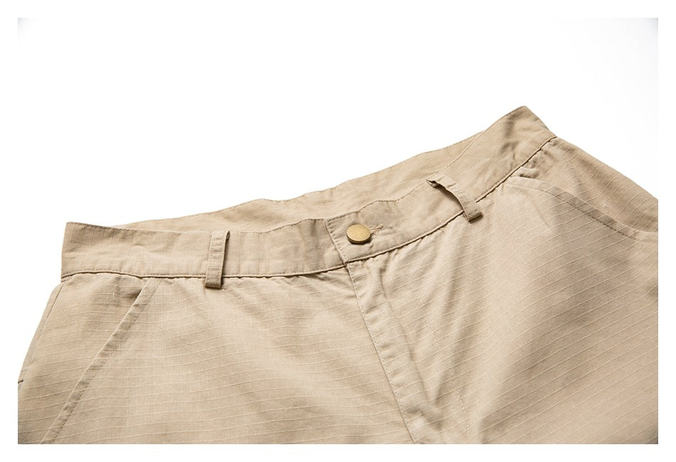 Close-up of the tan shorts waistband with belt loops, a button closure, and front pocket seams.