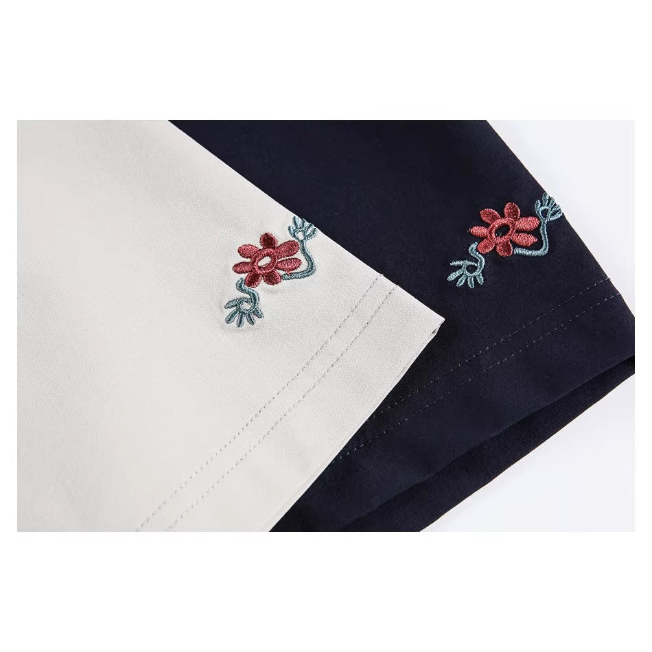 Close-up of beige and navy T-shirt sleeves with matching embroidered red flowers and teal stems.