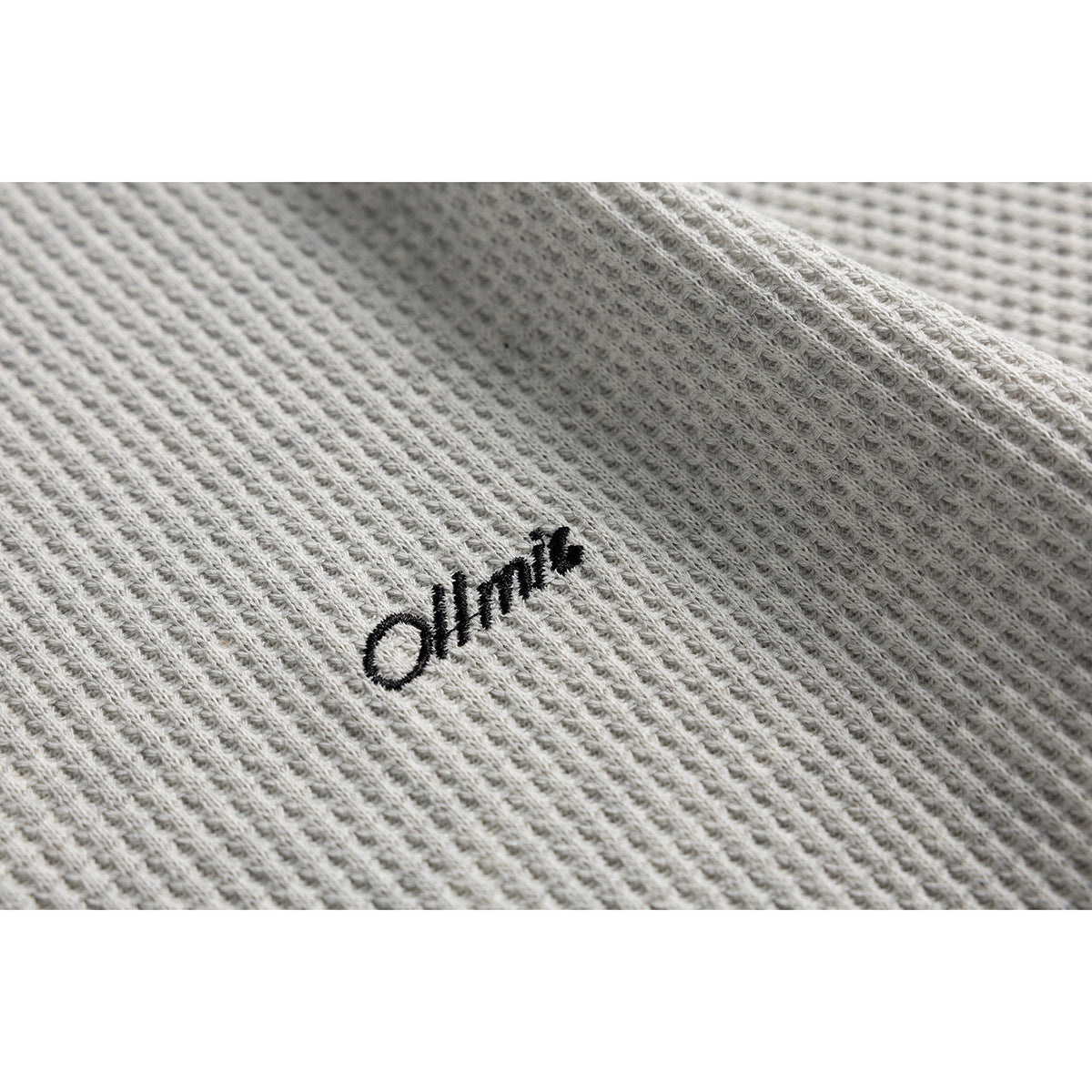Close-up of black embroidered lettering on light gray textured fabric.