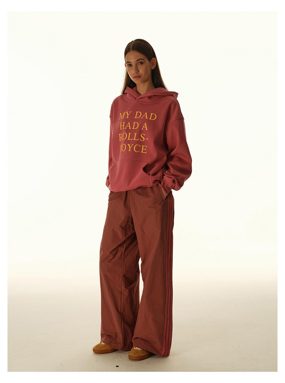 Model wearing a dusty rose hoodie with yellow lettering and loose rust-colored track pants.