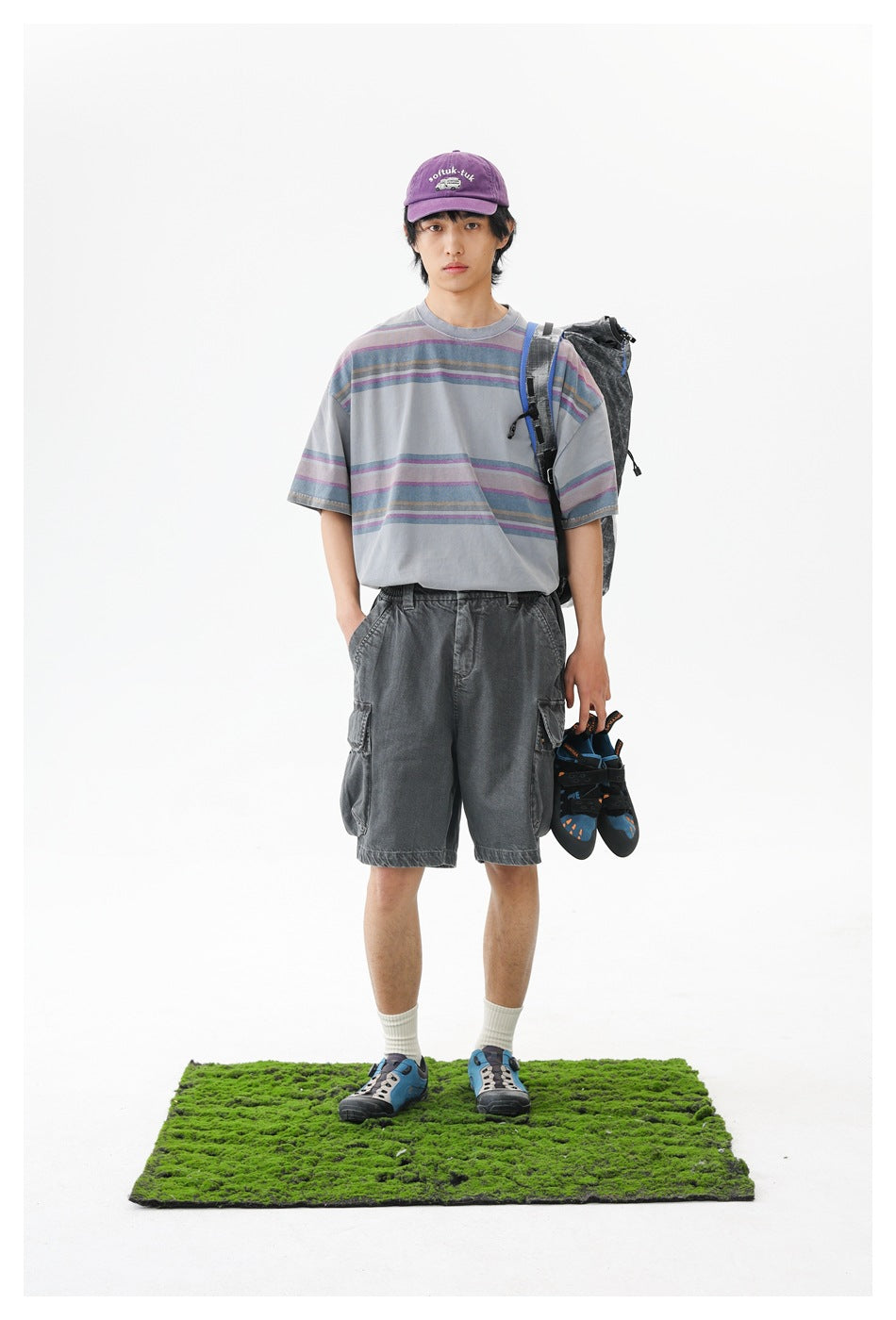 Front view of a model wearing a gray striped T-shirt and charcoal cargo shorts, with a backpack and climbing shoes.