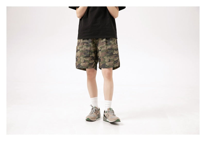 Front view of a model wearing camouflage shorts with a black T-shirt and gray sneakers.