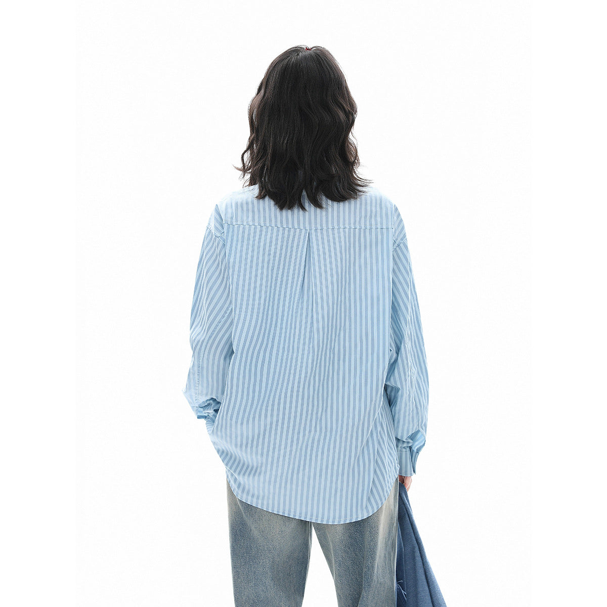 Back view of a model wearing an oversized light blue and white striped shirt with a curved hem.