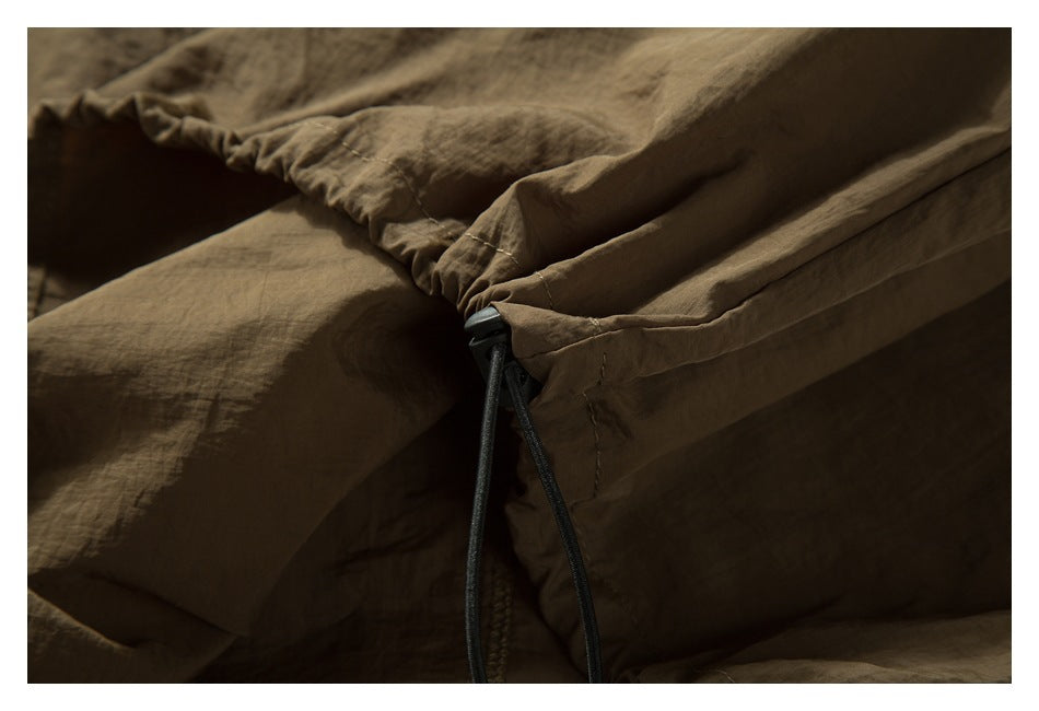 Close-up of a brown garment's gathered seam with a black drawcord and toggle.