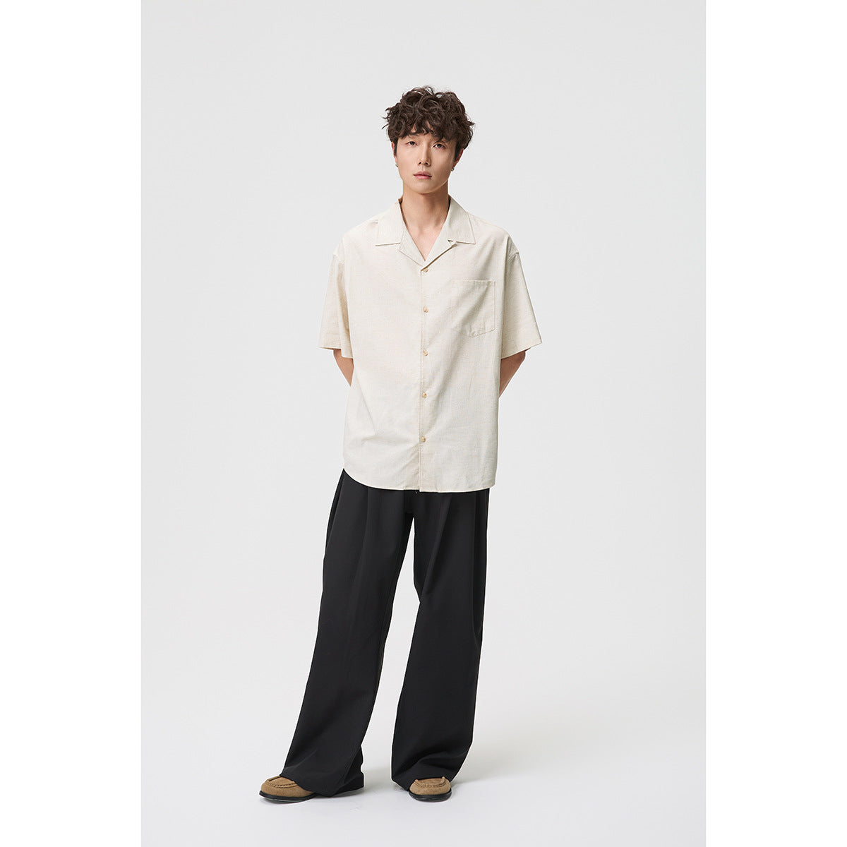 Full-length model wearing an off-white short-sleeve button-up shirt with a chest pocket and wide black trousers.