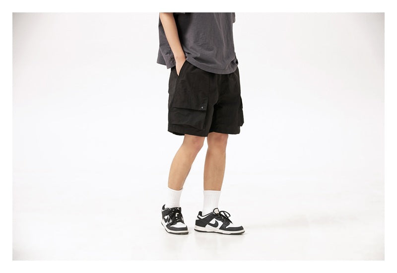 Model wearing black cargo shorts with flap pockets, a dark gray T-shirt, white socks and sneakers.