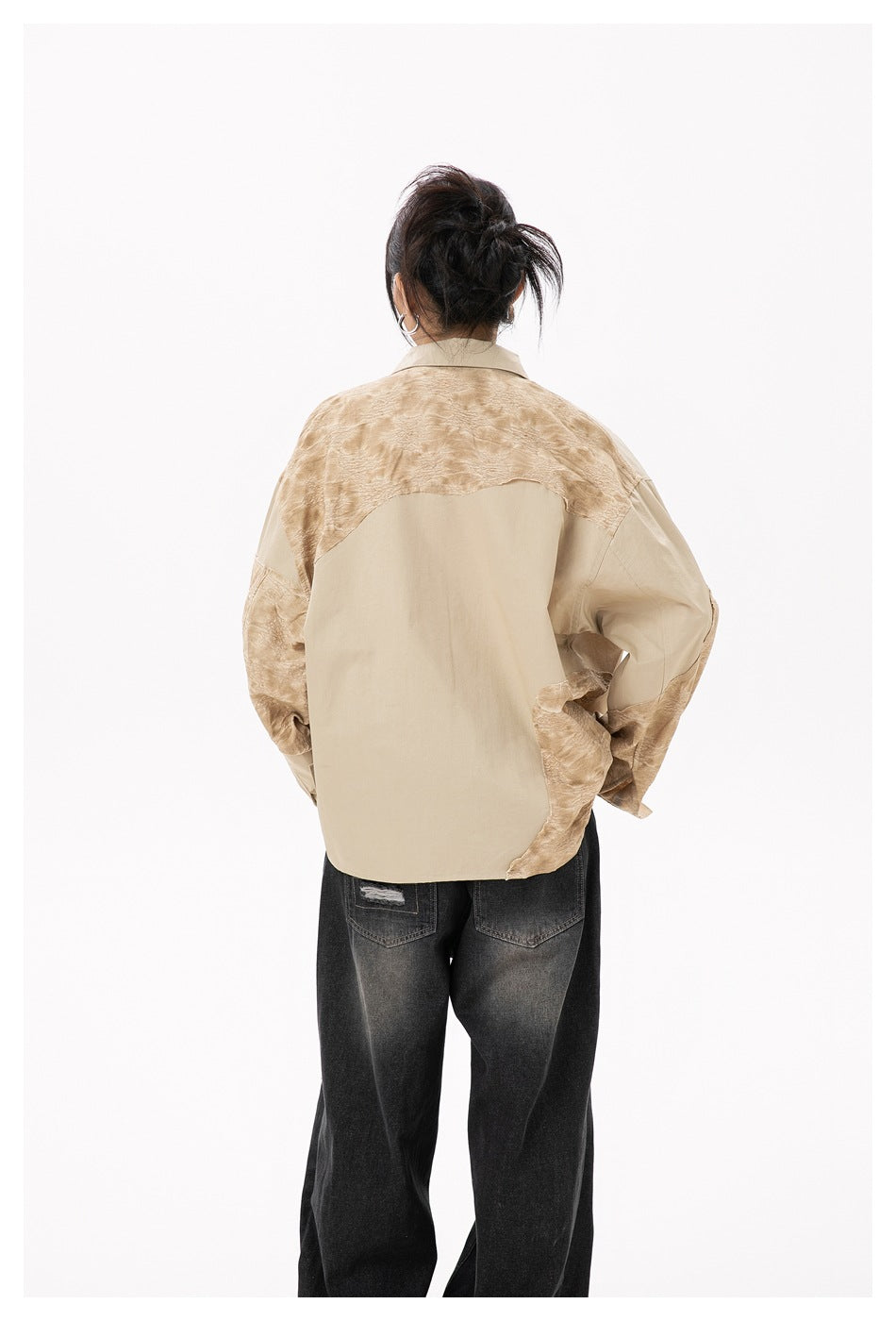 Back view of a model wearing a loose beige shirt with tan textured panels across the shoulders and sleeves.