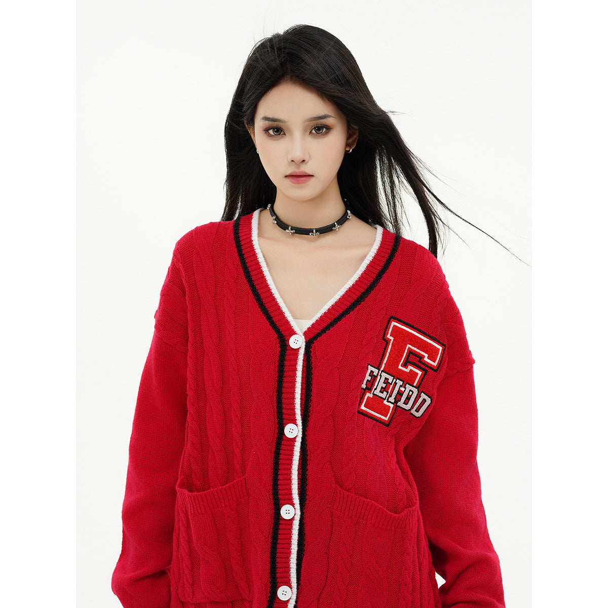 Close view of a model wearing a red cable-knit cardigan with striped V-neck trim, white buttons and a letter patch.