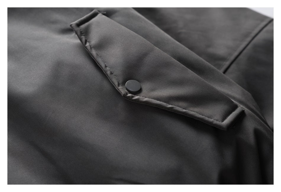 Close-up of a charcoal jacket's angled snap-button pocket flap and smooth fabric.