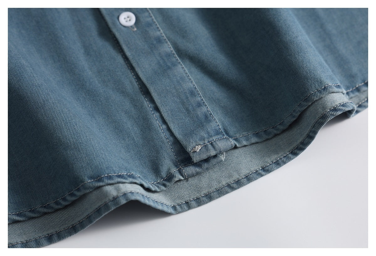 Close-up of a blue denim shirt's button placket and curved, stitched hem.