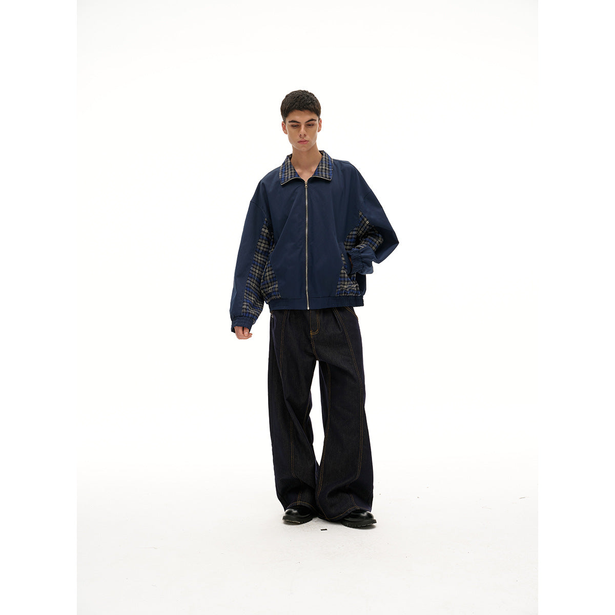 Full-length view of a model wearing a navy zip-front jacket with plaid collar and panels, paired with wide black jeans.