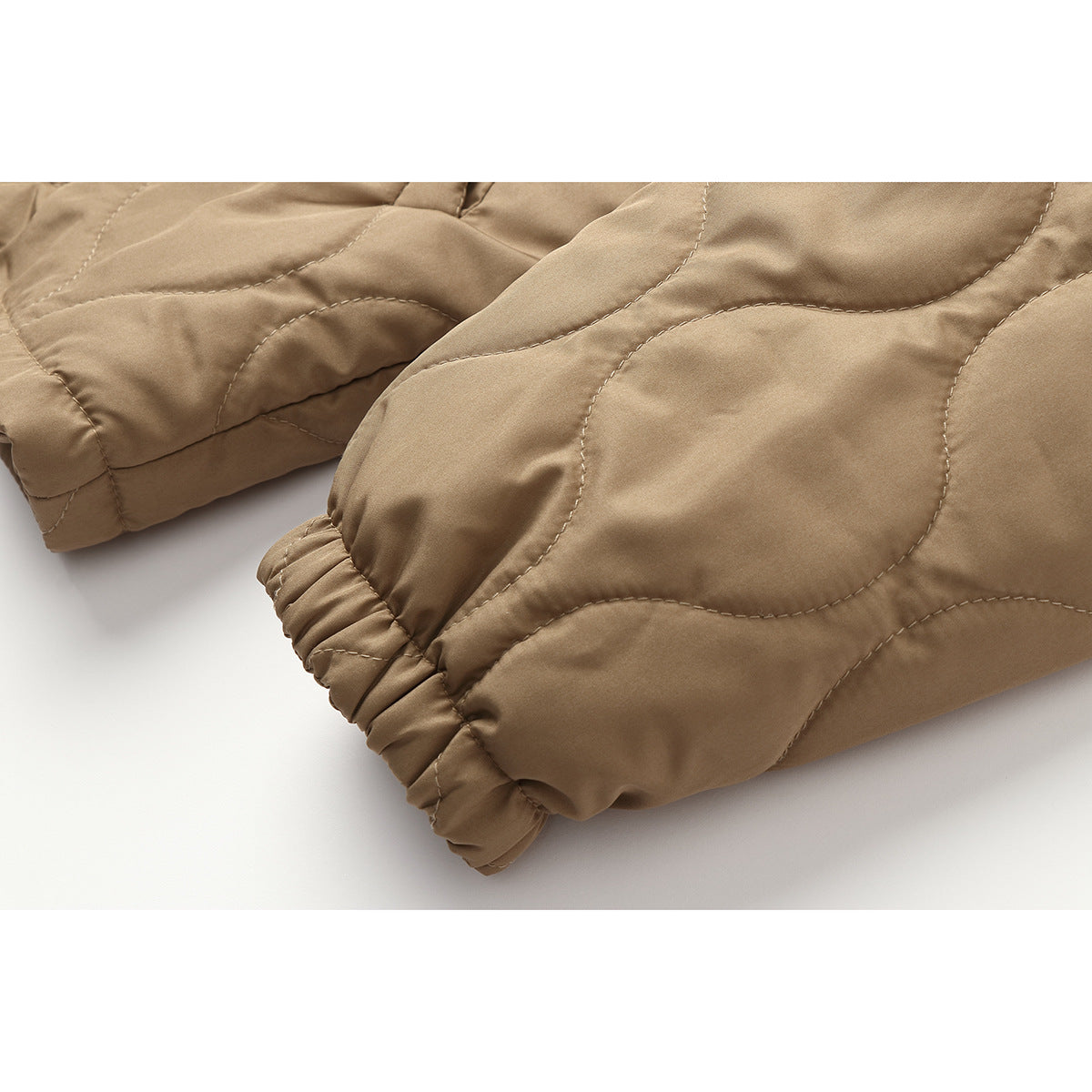 Close-up of tan quilted jacket sleeves with curved stitching and elastic cuffs.