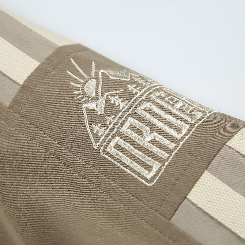 Close-up of a cream embroidered mountain-and-lettering graphic on the taupe jacket sleeve between cream stripes.