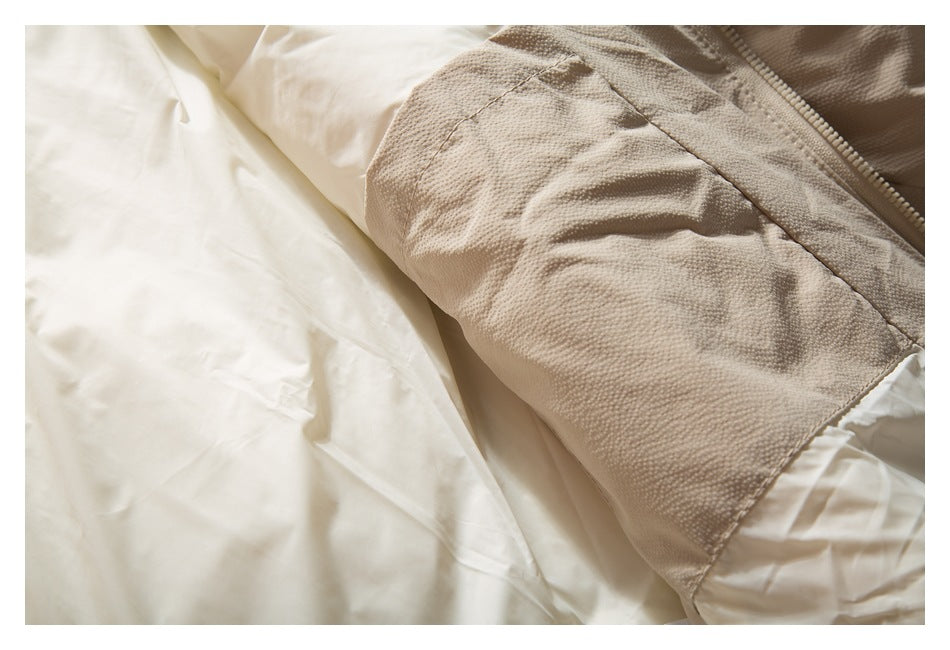 Close-up of a beige textured garment panel with a curved seam and zipper beside white fabric.