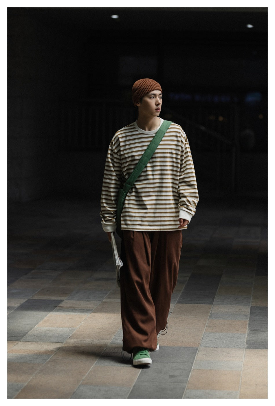 Model walking in brown wide-leg trousers, a cream-and-brown striped shirt, and a rust beanie.