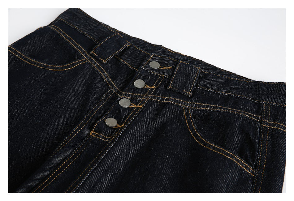 Close-up of dark indigo jeans showing the waistband, belt loops, four-button fly and contrast stitching.