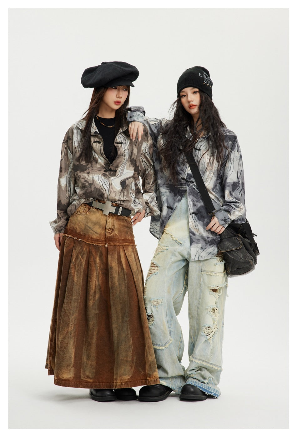 Two models wear oversized abstract-pattern shirts in brown and gray, styled with a long brown skirt and distressed jeans.