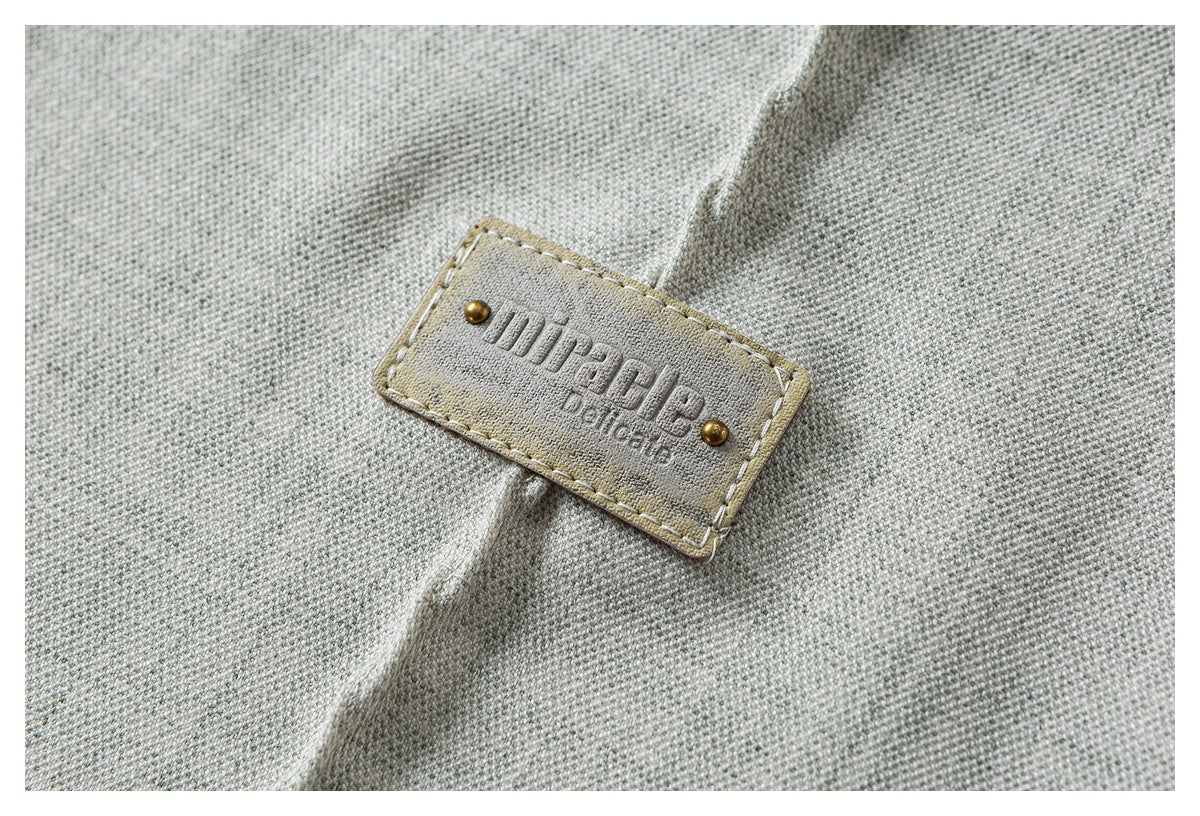 Close-up of a light gray woven shirt with a stitched rectangular embossed label.