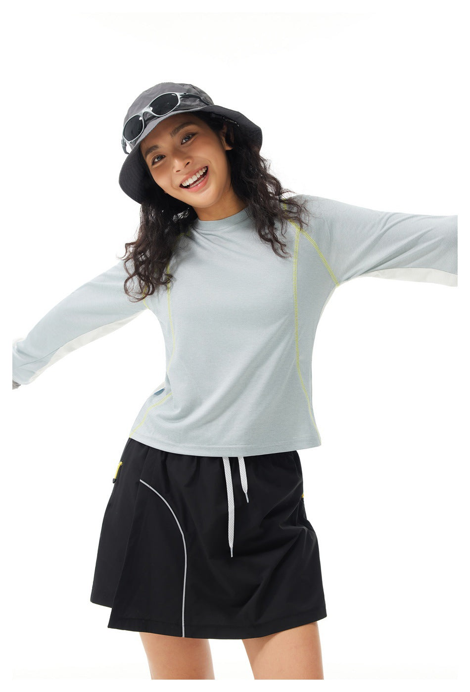 Model wearing a pale gray long-sleeve top with lime seam details and a black skort, arms outstretched.