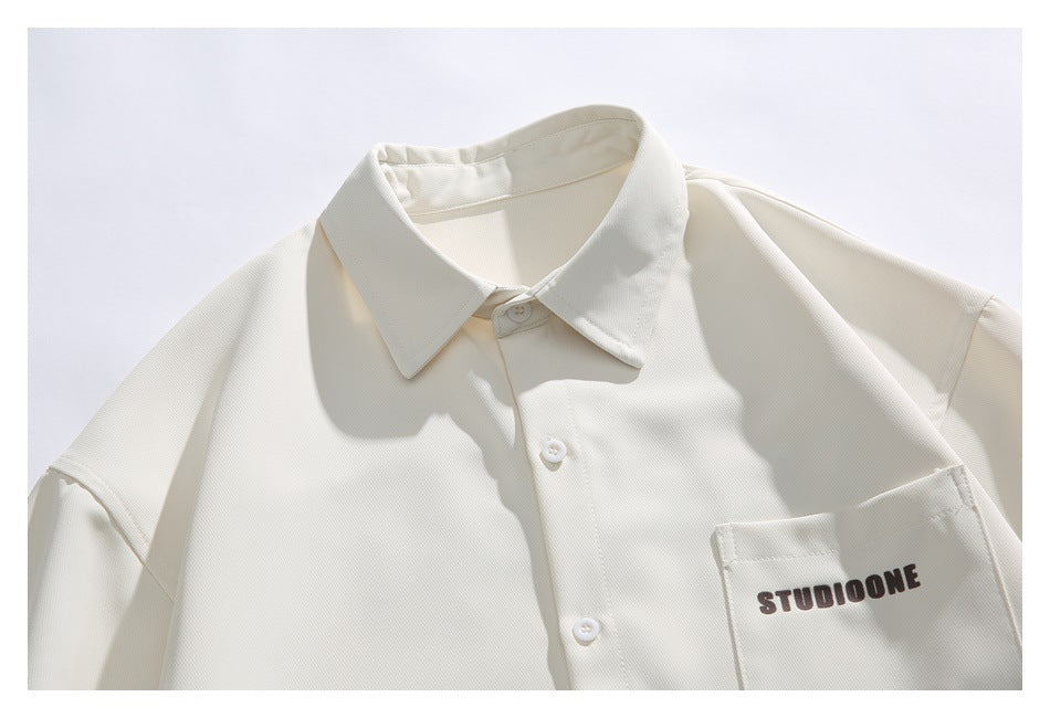 Close-up of an ivory shirt's pointed collar, front buttons, and chest pocket with dark lettering.