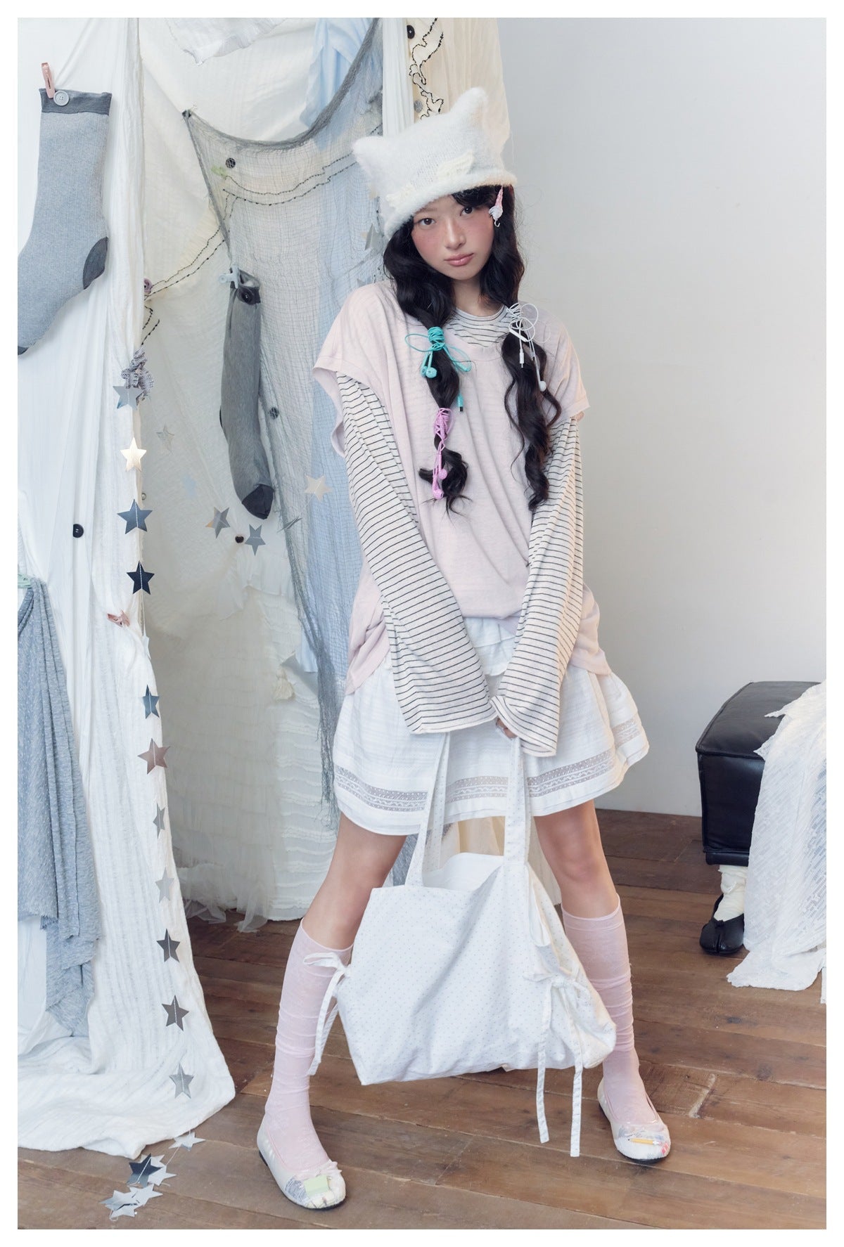 Full-length model wearing a pale pink top over a striped shirt, a white skirt, and pale pink knee-high socks.