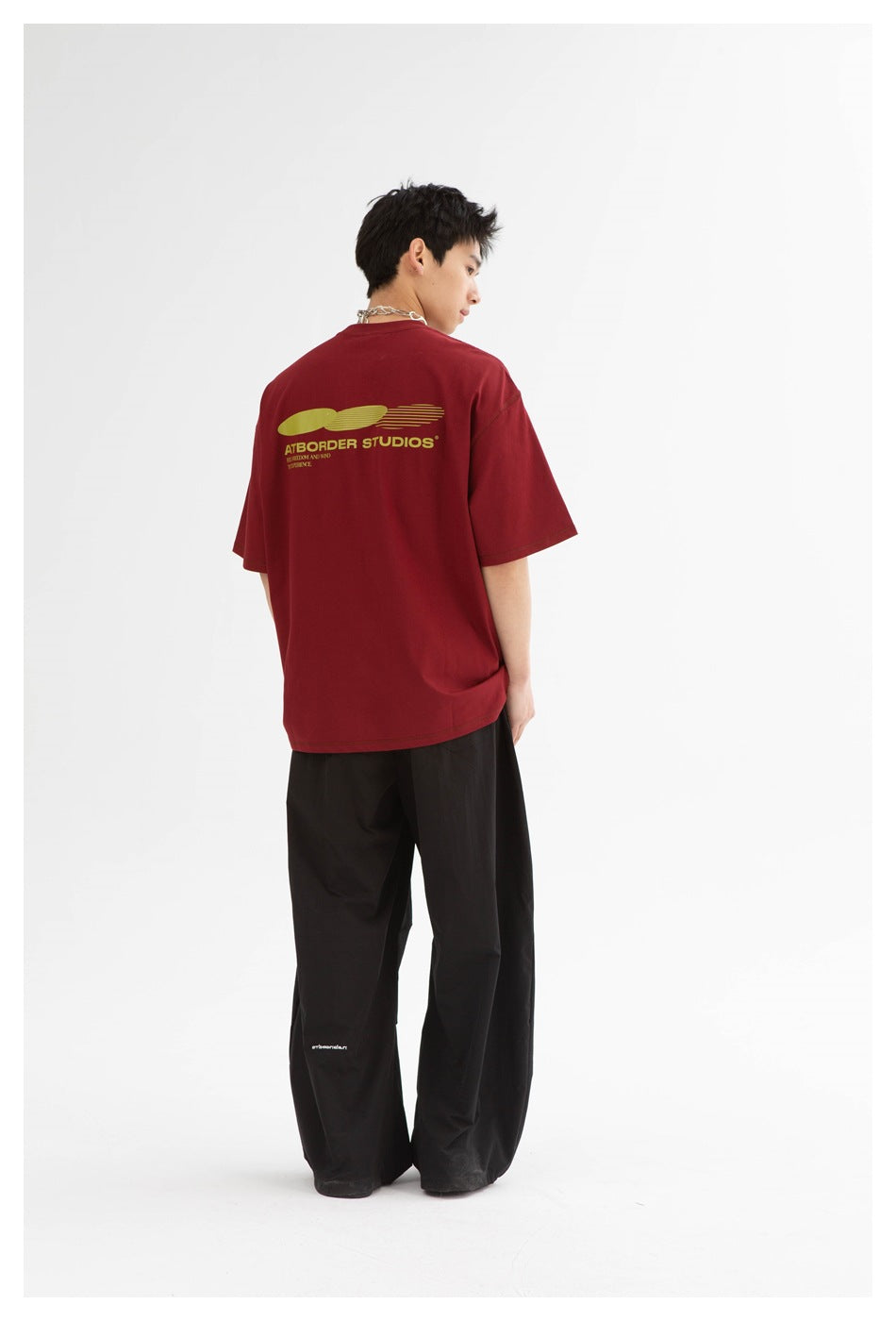 Model viewed from behind wearing a burgundy oversized T-shirt with a yellow back graphic.