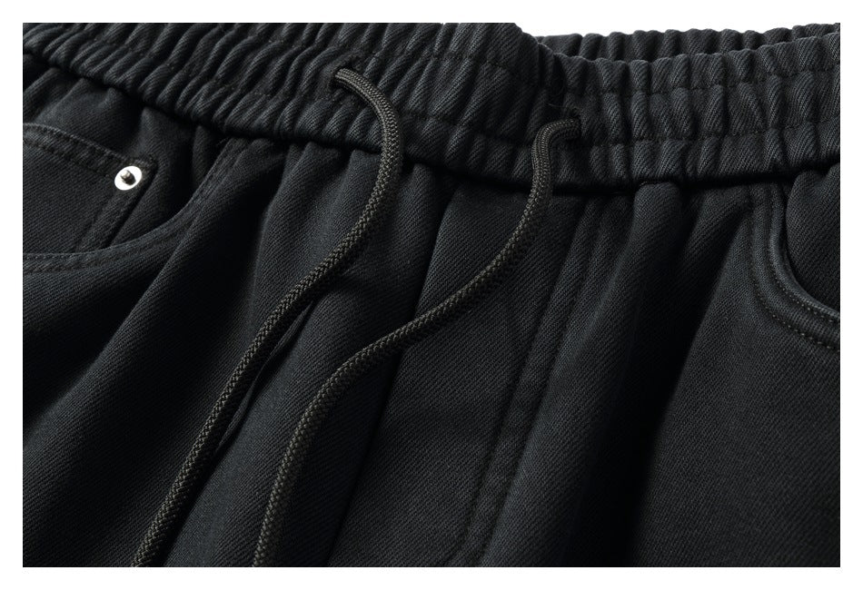 Close-up of black pants showing the gathered elastic waistband, two drawstrings and front pocket edges.