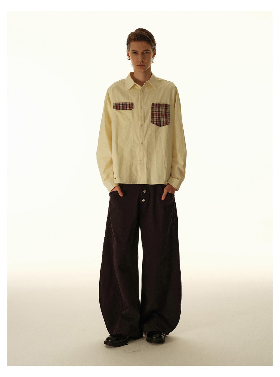 Full-length model wearing a cream button-up shirt with plaid chest pockets and wide dark trousers.