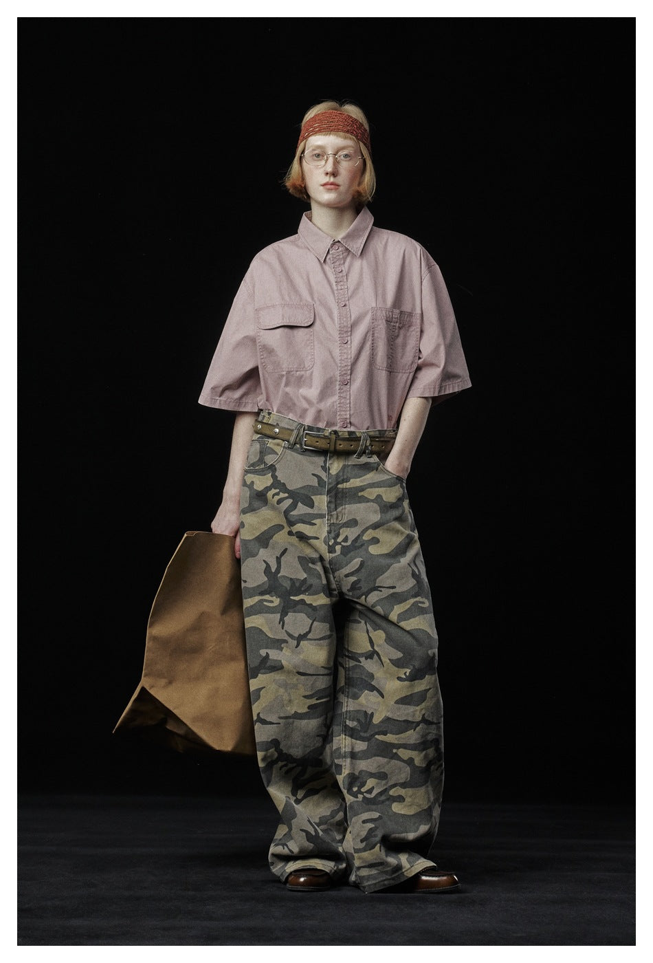 Model wearing a dusty pink short-sleeve shirt with two chest pockets and loose camouflage trousers.