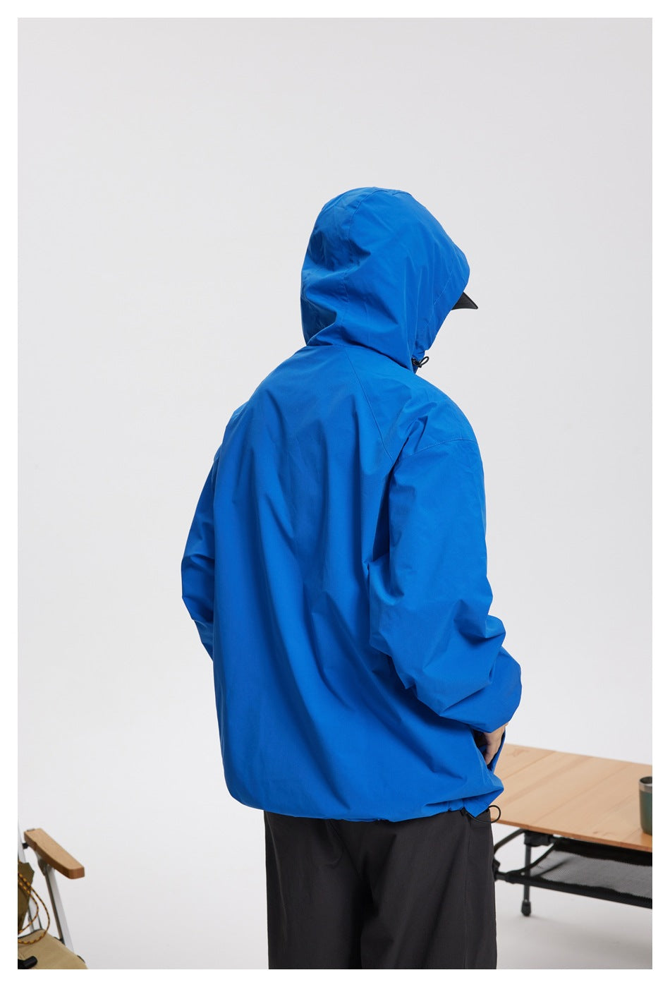 Rear view of a person wearing a bright blue hooded jacket and black trousers.