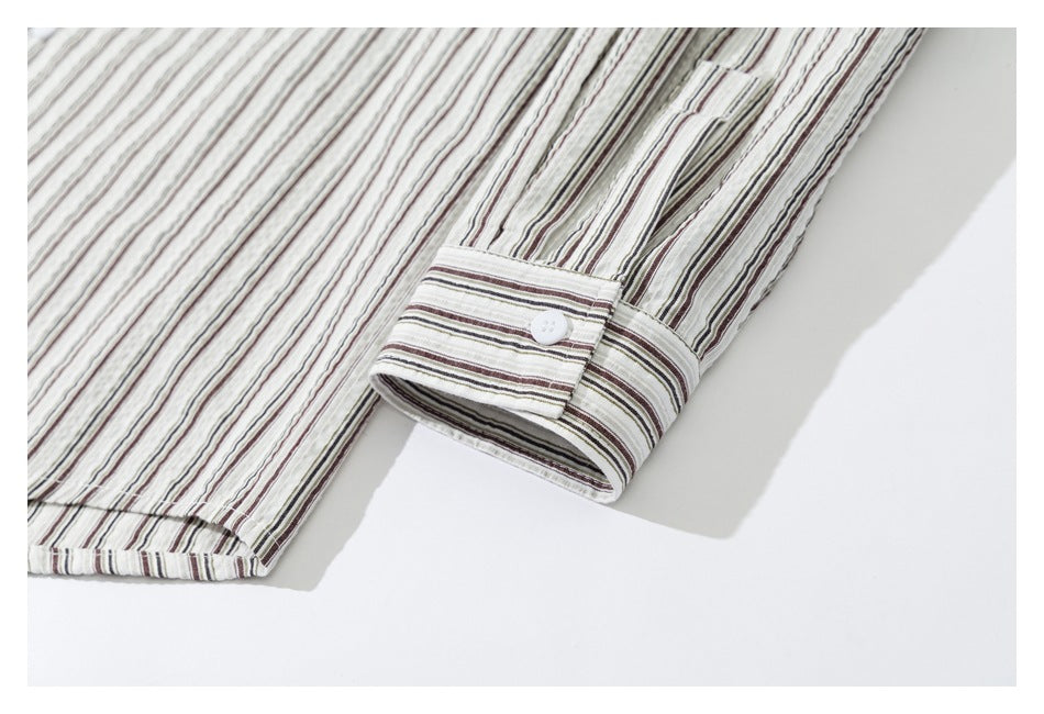 Close-up of a white shirt cuff with a white button and hem, in thin brown, gray, and olive stripes.