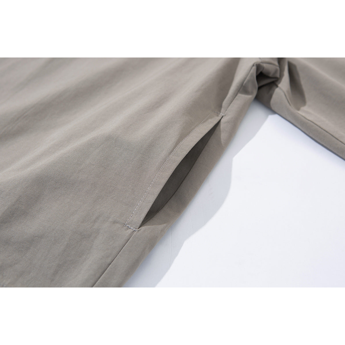 Close-up of the taupe jacket's angled side pocket and stitched opening.
