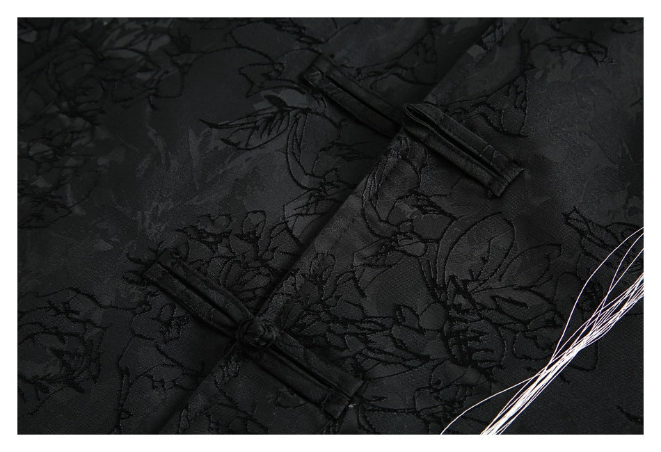 Close-up of black floral-patterned fabric with two black frog closures and white threadlike marks at the edge.