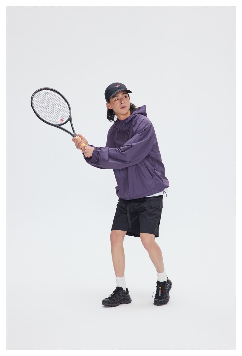 Person wearing a purple hooded jacket and black shorts while holding a tennis racket.