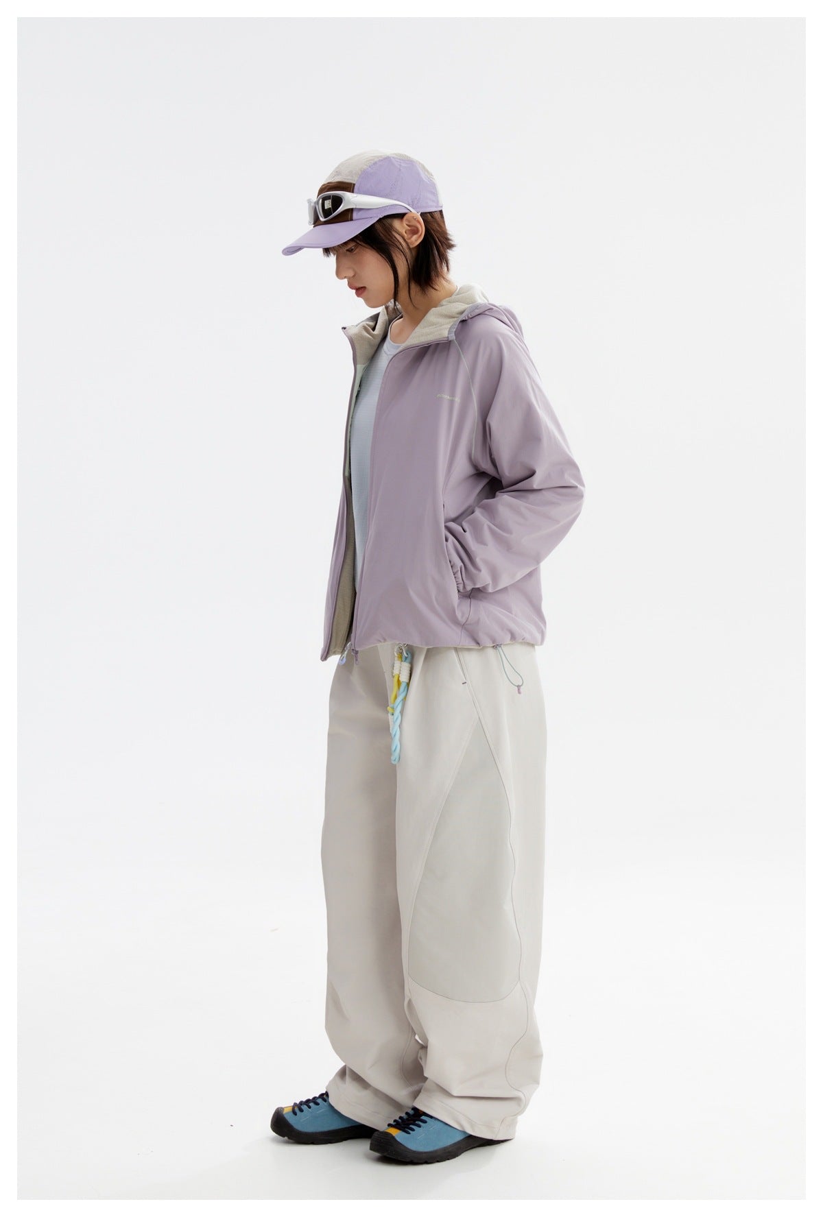 Side view of a model wearing a lavender hooded zip jacket and loose light trousers.