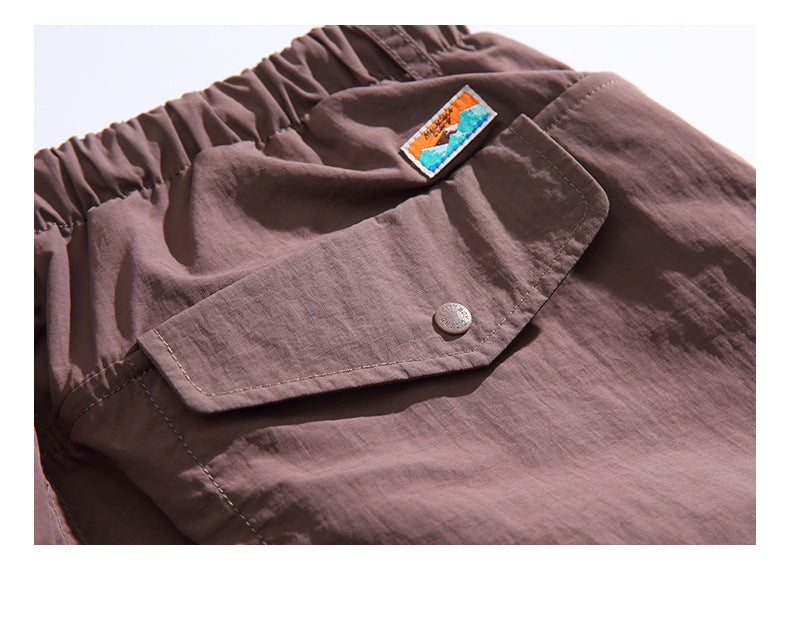 Close-up of a brown shorts pocket with a buttoned flap and a small colorful sewn-on patch.