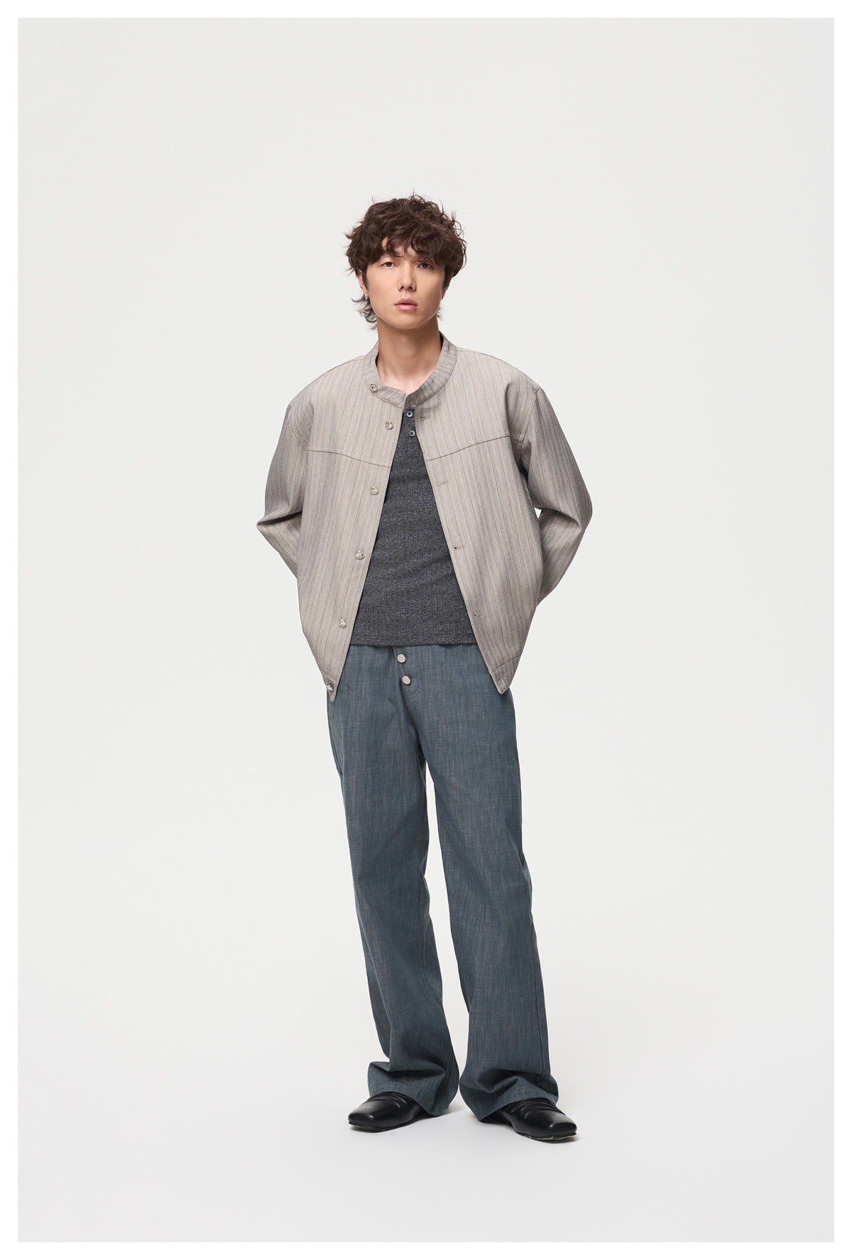 Full-length model wearing a light gray pinstriped, collarless button jacket with a dark shirt and wide blue trousers.