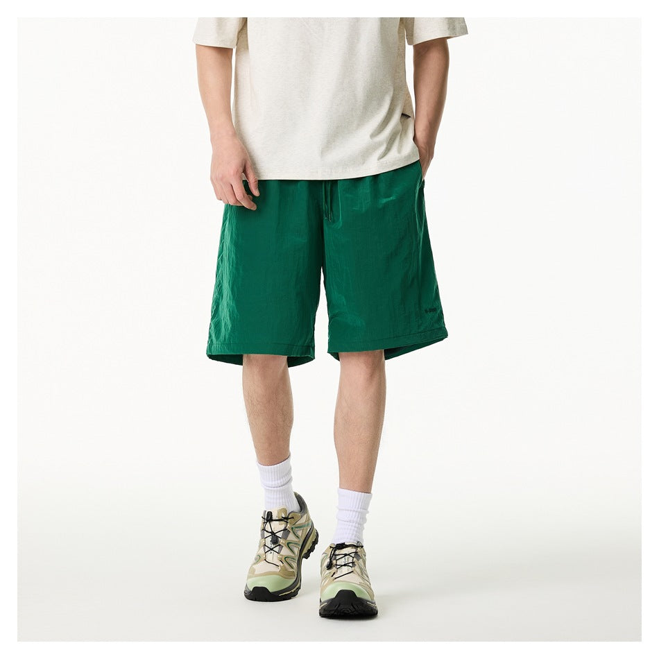 Model wearing green knee-length shorts with a light heather tee and white socks, front view
